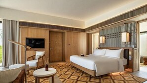 Quarto de hotel com cama, televisão, área de estar e tapete estampado.