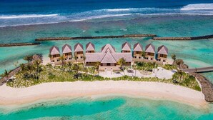 Um resort sobre as águas com vários edifícios tipo bangalô, uma praia de areia e águas turquesa cristalinas.