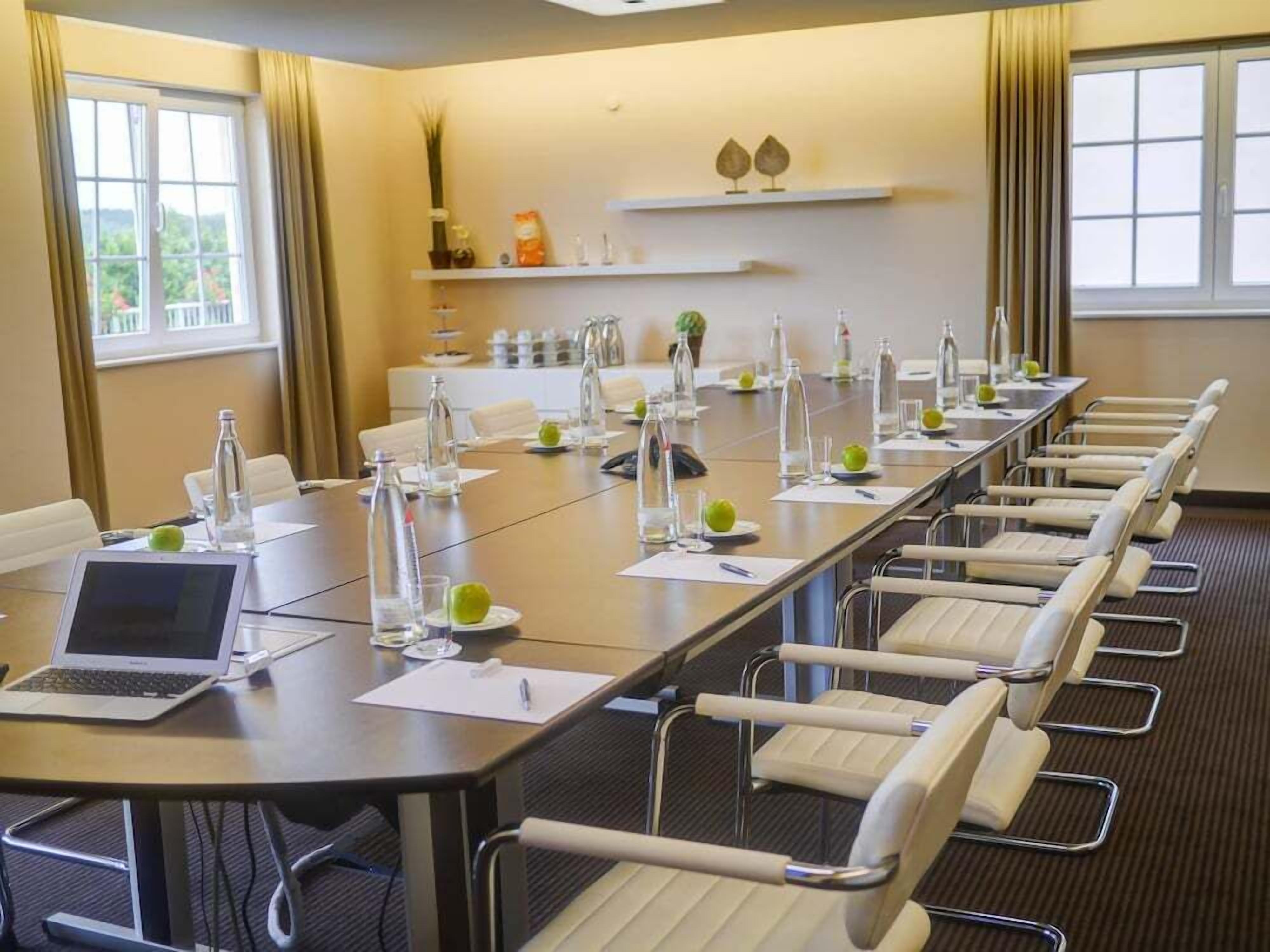 A conference room with a long table, chairs, a laptop, water bottles, and a plant on the wall.