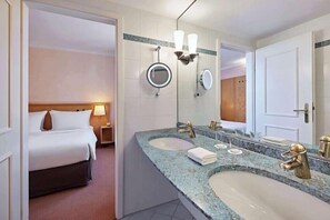A hotel room with a bed, two sinks, a large mirror, and a nightstand. - Lindner Hotel Wiesensee (Stahlhofen am Wiesensee)
