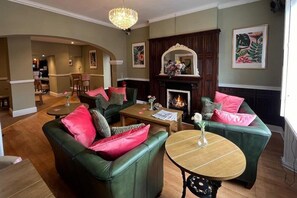 A living room with green sofas, a fireplace, and a chandelier. - OYO Rothwell House Hotel (Kettering)
