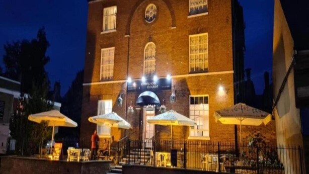 A brick building with a clock, outdoor seating with umbrellas, and a sign that reads 'Hotel Restaurant.' - OYO Rothwell House Hotel (Kettering)