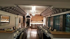 A long dining table set for a meal, with chairs on both sides, a chandelier above, and a brick wall in the background. - OYO Rothwell House Hotel (Kettering)