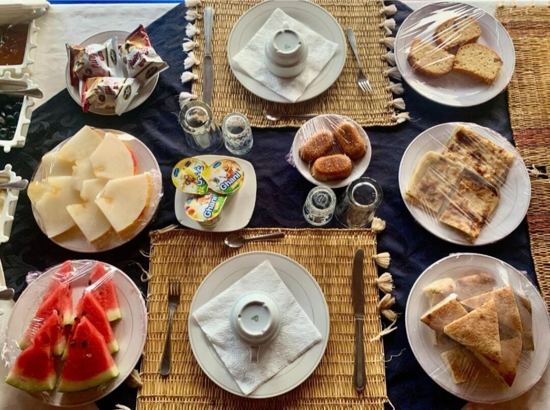 A table set with various food items and condiments, including sliced bread, cheese, and a plate of watermelon slices.