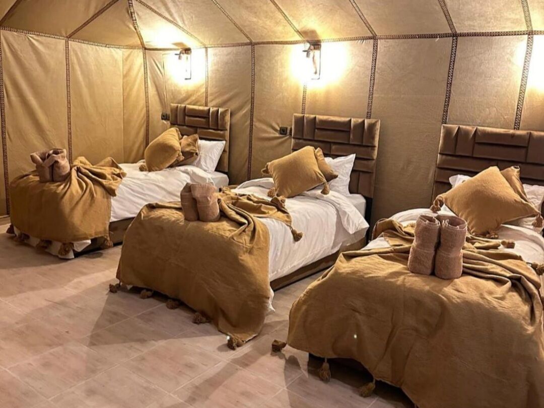 Ein Zelttraumzimmer mit drei Betten, jeweils mit Kopfteil und Kissen.