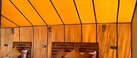 A tented room with two beds, wooden headboards, and hanging lanterns.
