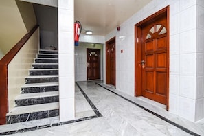 Un pasillo con suelo de mármol, puertas de madera y una escalera.