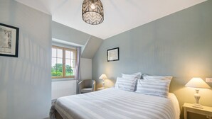 A bedroom with a bed, two bedside tables, a chair, a window, and a ceiling light fixture. - Bed and Breakfast 'Chambre Chausey' with Shared Terrace, Shared Garden and Wi-Fi (Muneville-sur-Mer)