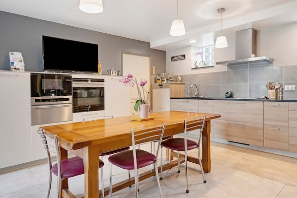 A modern kitchen with a wooden dining table, stainless steel appliances, and pendant lighting.