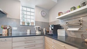 A modern kitchen with wooden cabinets, a black countertop, a coffee maker, a kettle, and a clock on the wall. - Bed and Breakfast 'Chambre Chausey' with Shared Terrace, Shared Garden and Wi-Fi (Muneville-sur-Mer)