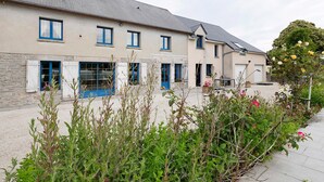 A building with multiple windows, a stone facade, and a garden area with plants and flowers. - Bed and Breakfast 'Chambre Chausey' with Shared Terrace, Shared Garden and Wi-Fi (Muneville-sur-Mer)