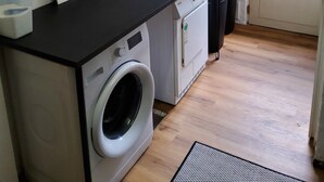 A compact laundry room with a washing machine, dryer, and ironing board. - Built in 1920, a house with a two-story sunroom, just a short drive from the North Sea  (Ostrohe)