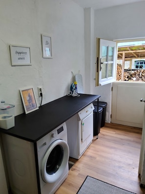 Een kleine wasruimte met een wasmachine, droger en een strijkplank.