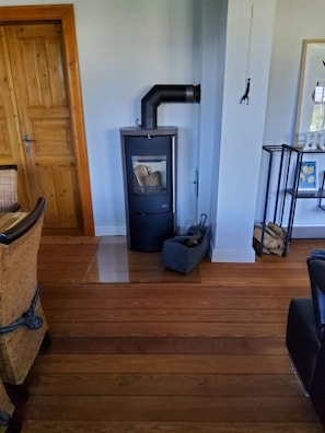 A room with a wood-burning stove, a wicker chair, a black chair, and a wooden door.