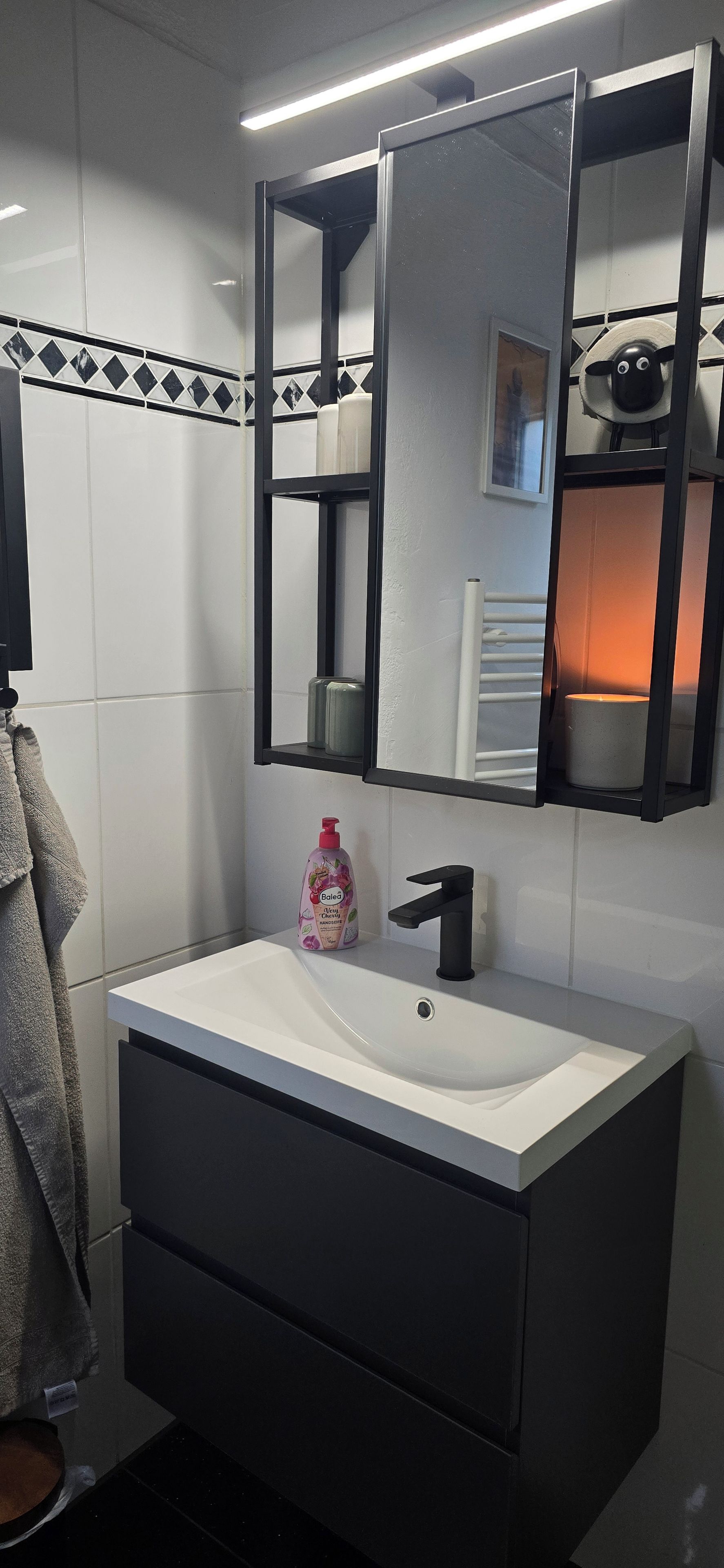 Une salle de bain avec un lavabo blanc, un robinet noir et un miroir au-dessus.