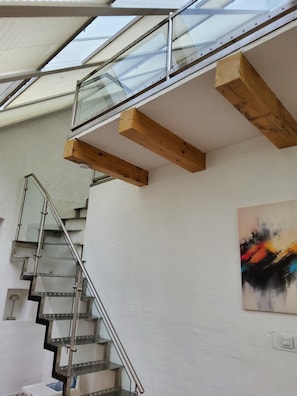 A modern interior with a glass staircase, wooden beams, and a colorful abstract painting.