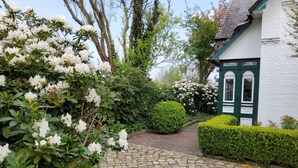A cobblestone pathway leading to a white building with green trim and a green door. - Built in 1920, a house with a two-story sunroom, just a short drive from the North Sea  (Ostrohe)