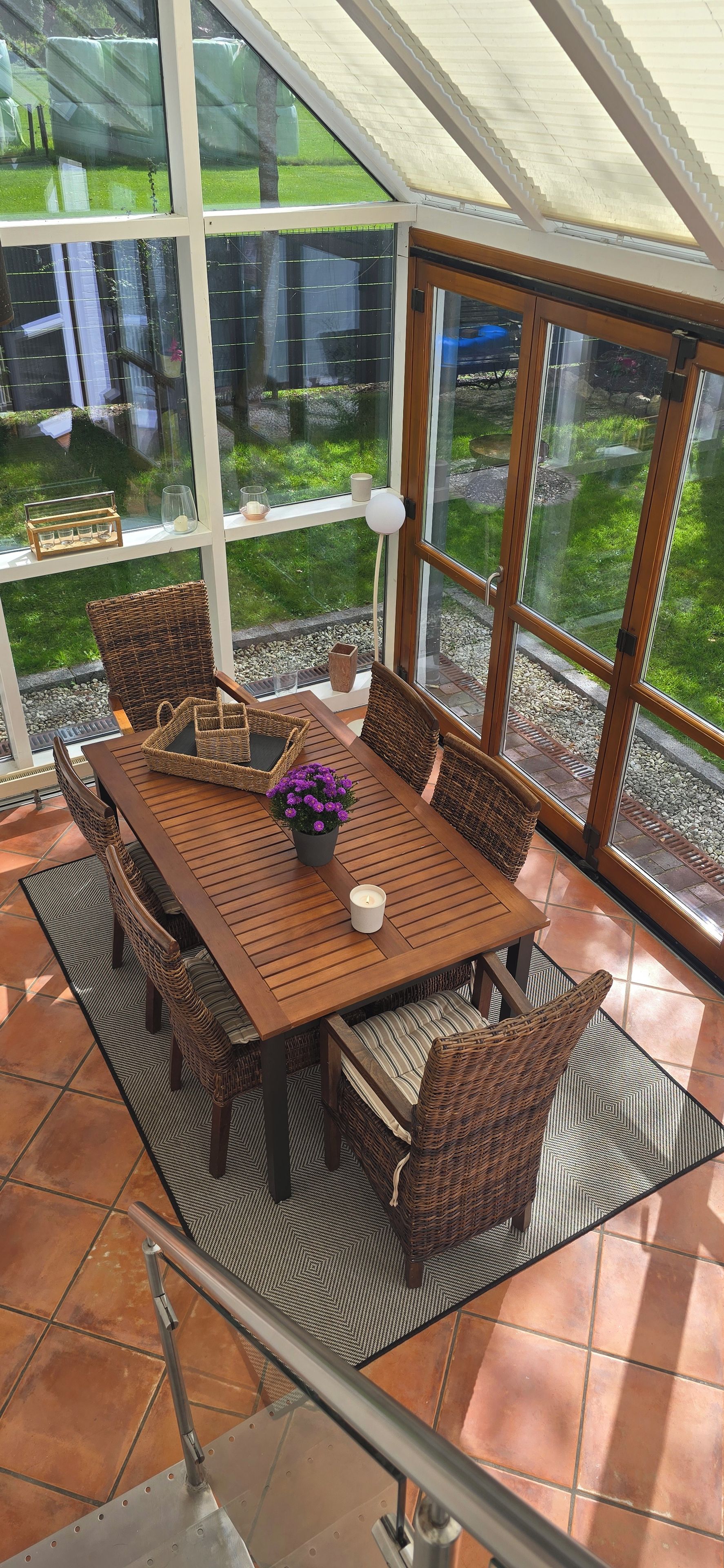 A sunlit patio with a wooden table, wicker chairs, and a potted plant.