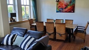 A living room with a black leather sofa, a dining table with wicker chairs, and a colorful abstract painting on the wall. - Built in 1920, a house with a two-story sunroom, just a short drive from the North Sea  (Ostrohe)