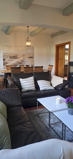 A modern living room with a sectional sofa, a coffee table, and a dining area with wicker chairs.