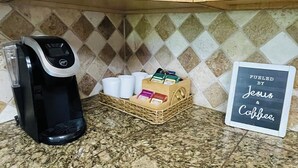 Una cuina amb una cafetera, tasses i un cartell que diu 'FUELED BY Jesus & Coffee'.