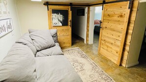Una habitació acollidora amb un sofà, una catifes, parets de fusta i una porta que dona a una altra habitació.