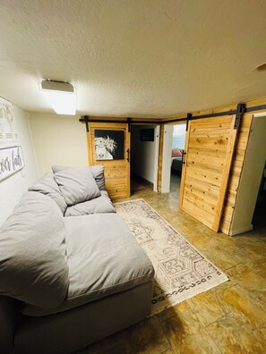 A cozy room with a sofa, a rug, wooden walls, and a door leading to another room.