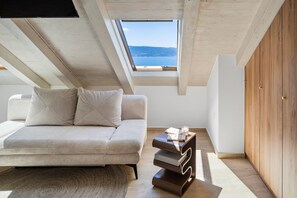 Ein modernes Schlafzimmer im Loft-Stil mit Schlafsofa, kleinem Nachttisch mit Kerze und Seeblick durch ein Dachfenster.