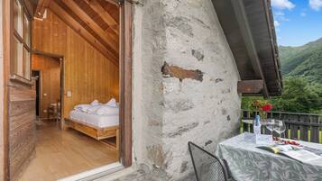 Una habitación de madera con una cama, un balcón con mesa y vistas a un paisaje montañoso.