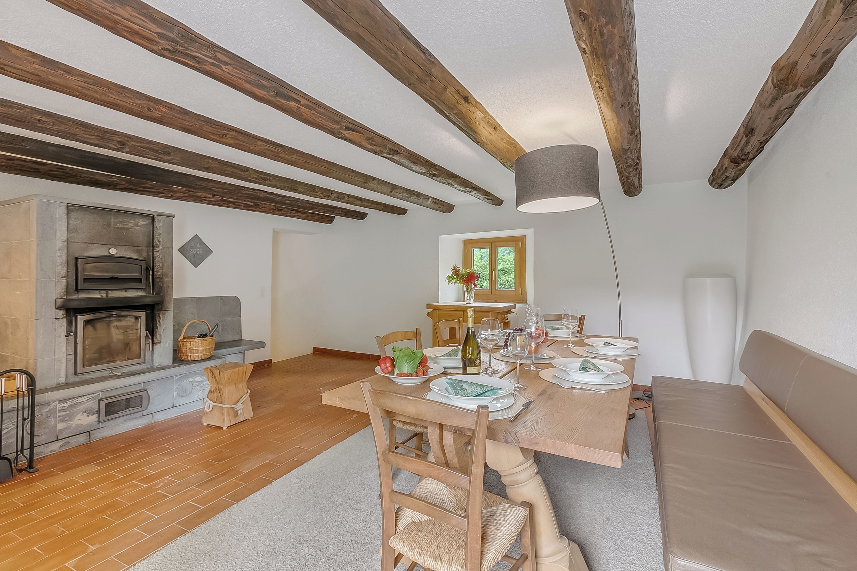 Comedor con mesa de madera para cuatro, chimenea y vistas al exterior.