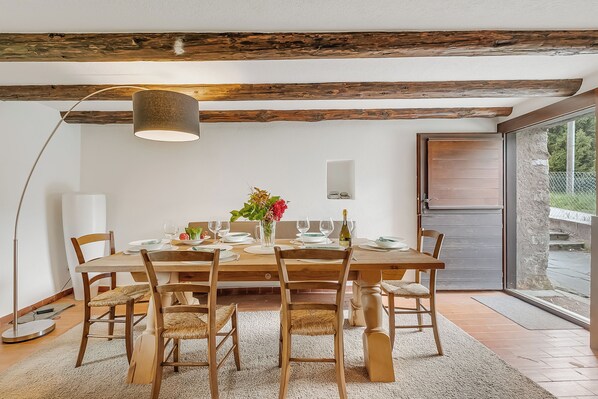 A dining area with a wooden table, chairs, a vase with flowers, and a lamp. - Casa Eyrie Centovalli 3BR Chalet (Centovalli)