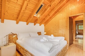 A wooden-paneled room with a bed, a nightstand, a lamp, and a door leading to another room. - Casa Eyrie Centovalli 3BR Chalet (Centovalli)