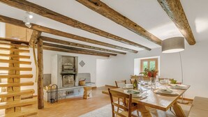 A dining area with a wooden table set for four, a fireplace, and exposed wooden beams.