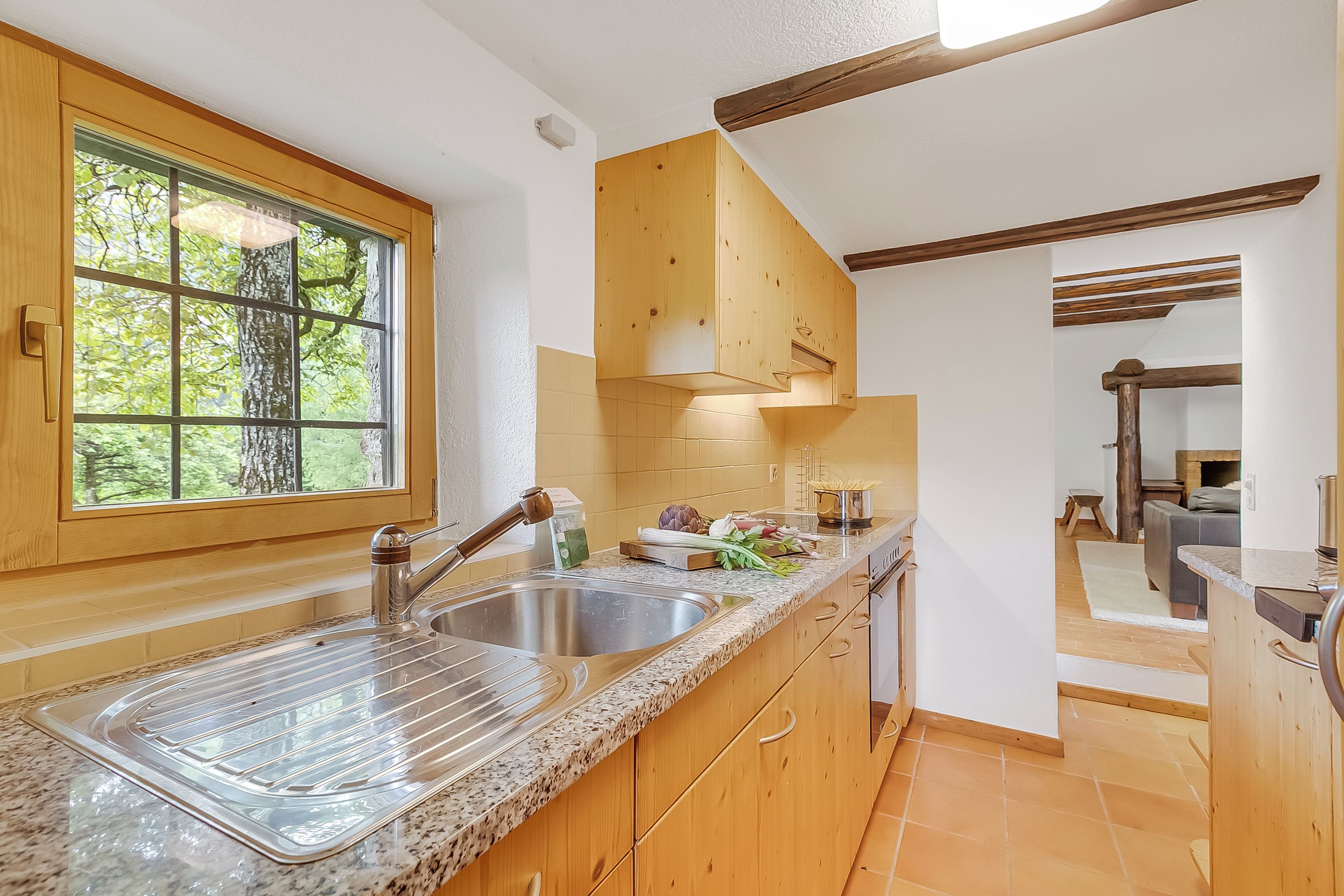 Una cocina con armarios de madera, encimera de granito, ventana con vistas a árboles y horno empotrado.
