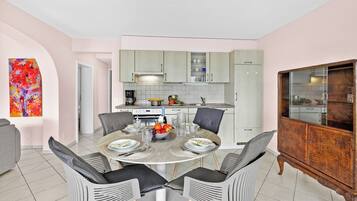 A modern kitchen with light-colored cabinets, a dining table with chairs, and a large wooden cabinet.