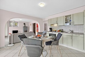 A modern kitchen with a dining area, featuring a central island, light-colored cabinets, and a tiled backsplash. - Panoramic Garden Lake View in Locarno Monti (Locarno)