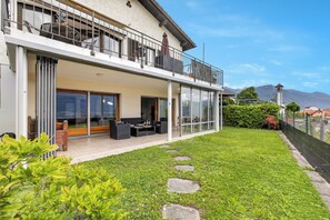 A two-story house with a balcony, a patio with outdoor furniture, and a well-maintained lawn. - Panoramic Garden Lake View in Locarno Monti (Locarno)