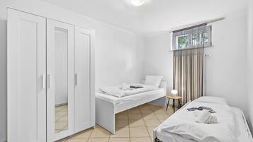A bedroom with a bed, a wardrobe, a small table with a lamp, and a window with curtains.