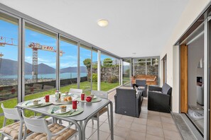 A modern dining area with a table set for two, large windows, and a view of a construction site. - Panoramic Garden Lake View in Locarno Monti (Locarno)
