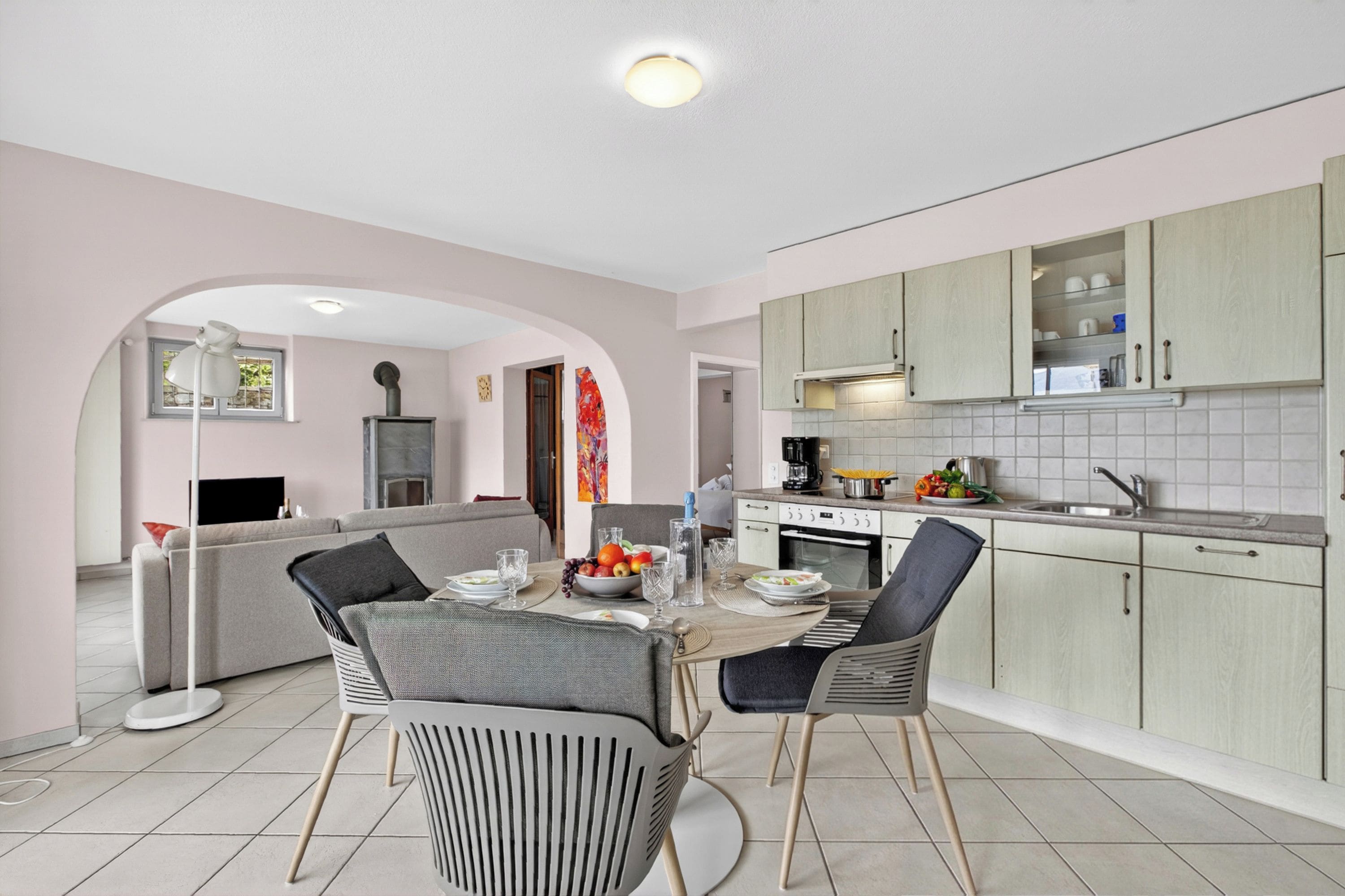 A modern kitchen with a dining area, featuring a central island, light-colored cabinets, and a tiled backsplash.