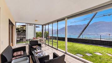 A spacious balcony with a dining area, large windows offering a view of mountains and a bridge, and a well-maintained lawn.