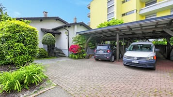 A building with a covered parking area, a white car, and a grey car parked in front.