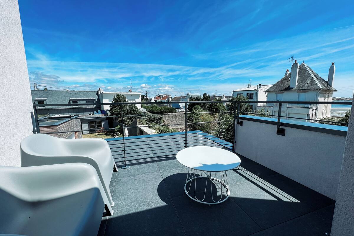 Une terrasse sur le toit, avec une table et des chaises, offrant une vue dégagée sur le paysage urbain et un ciel bleu.