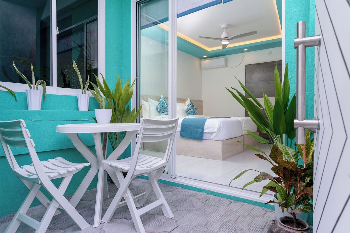 Una habitación con una cama, ventilador de techo y plantas en macetas.