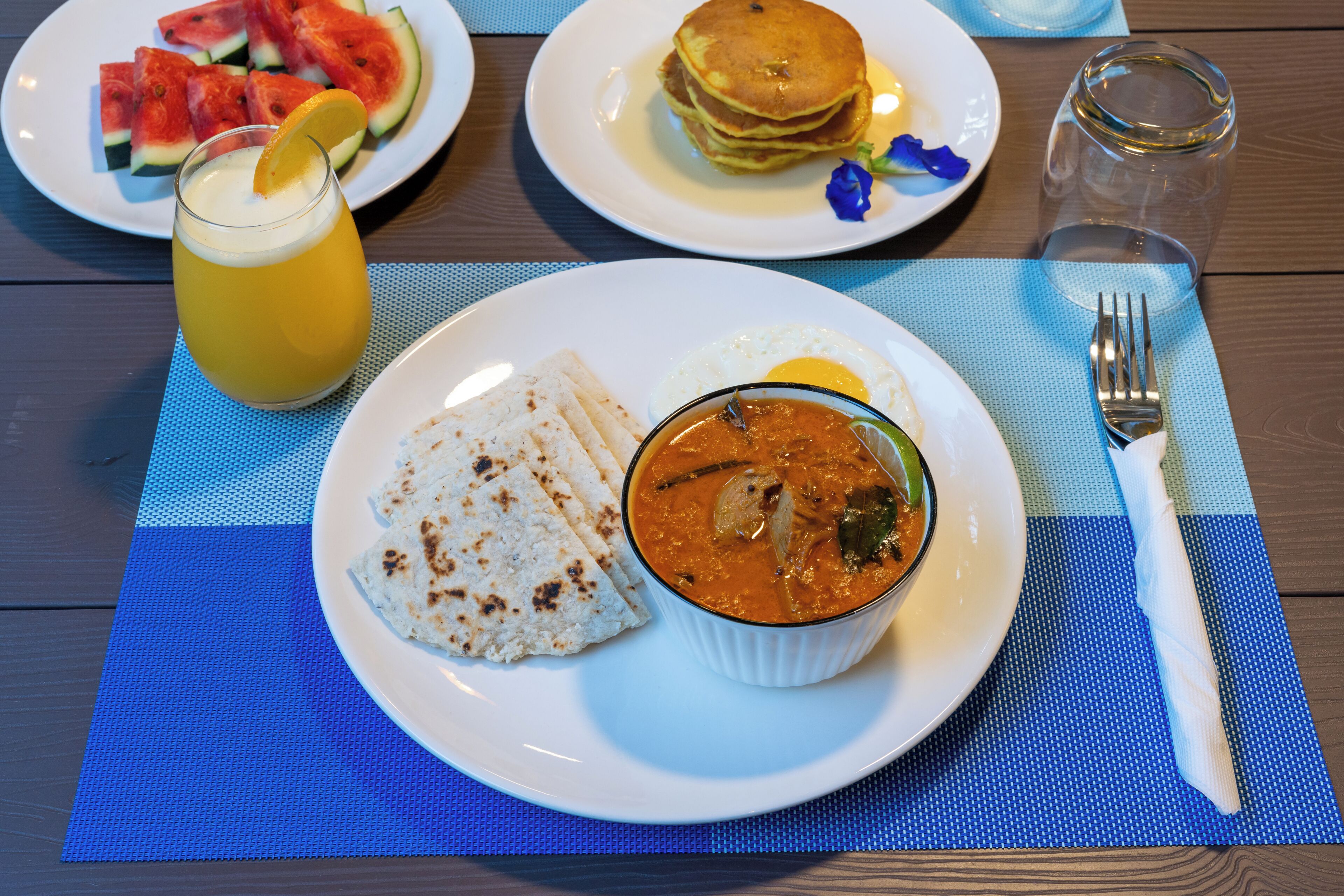 Un plato con curry, pan plano y un vaso de jugo sobre una mesa.