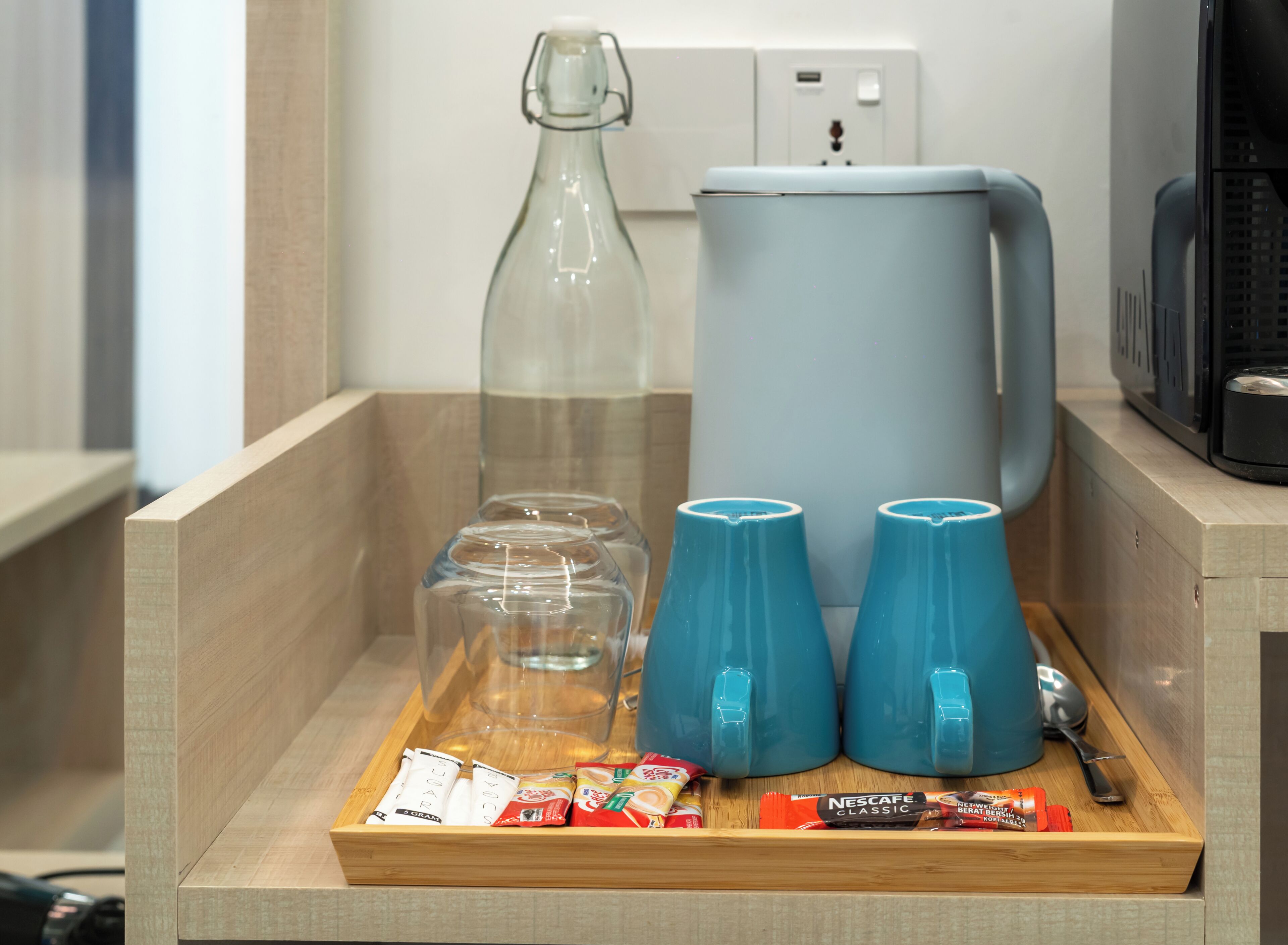 Un safata de fusta amb una ampolla de vidre, una cafetera, dues tasses blaves i alguns aliments envasellats.