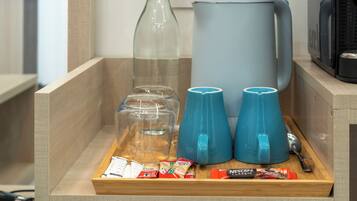 Un safata de fusta amb una ampolla de vidre, una cafetera, dues tasses blaves i alguns aliments envasellats.