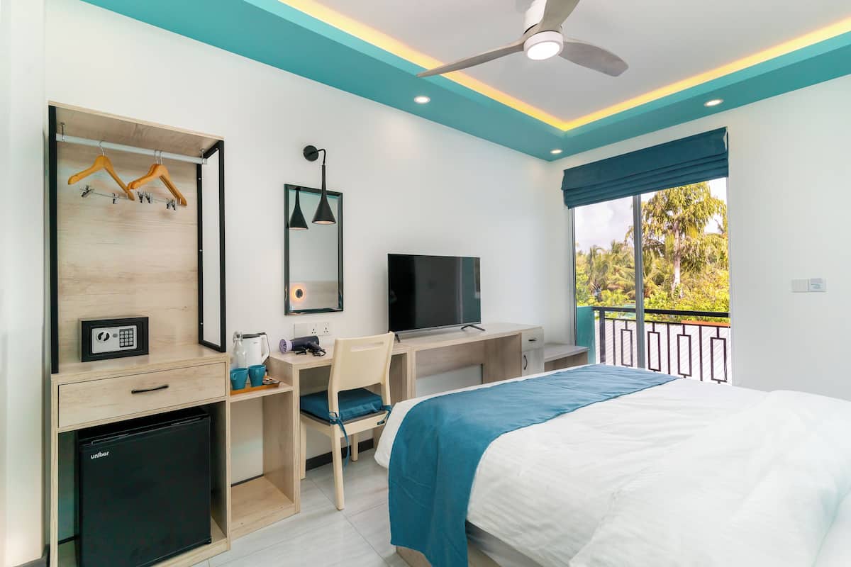 Habitación de hotel con cama, escritorio, silla, televisión, armario y balcón con vistas.