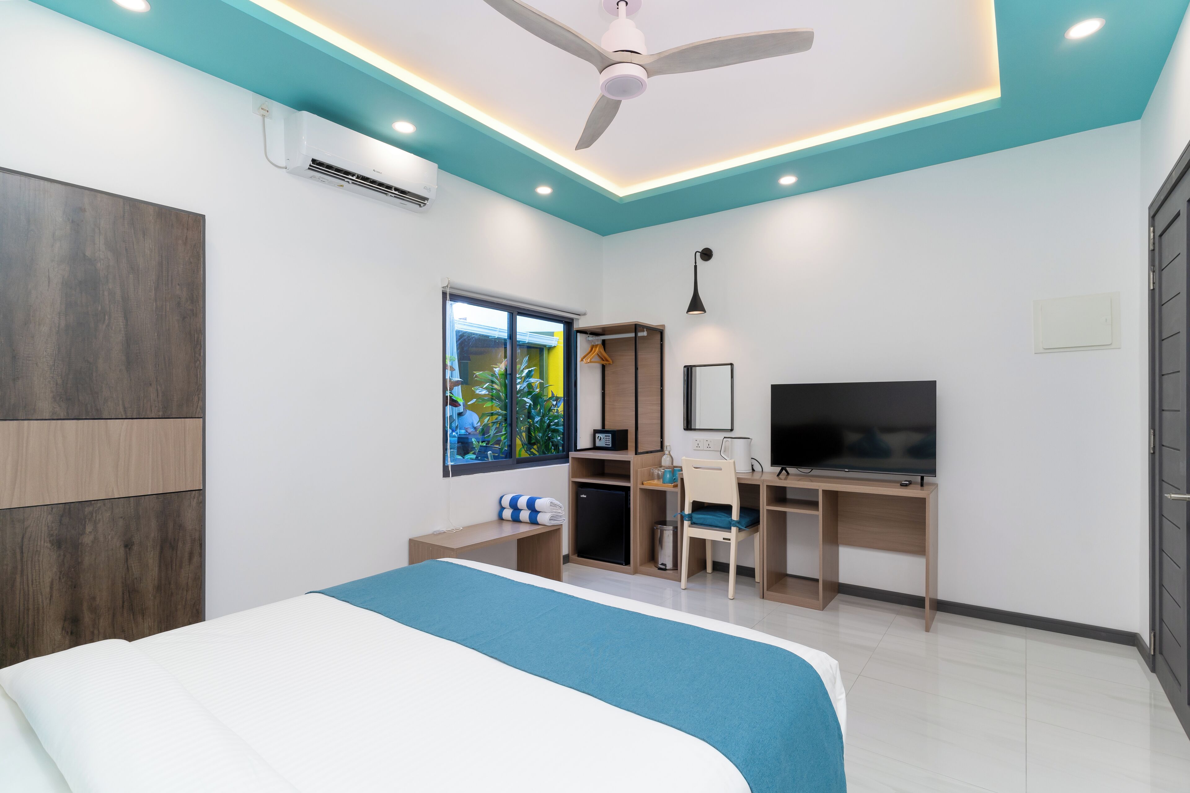 A bedroom with a bed, a desk, a TV, and a ceiling fan.