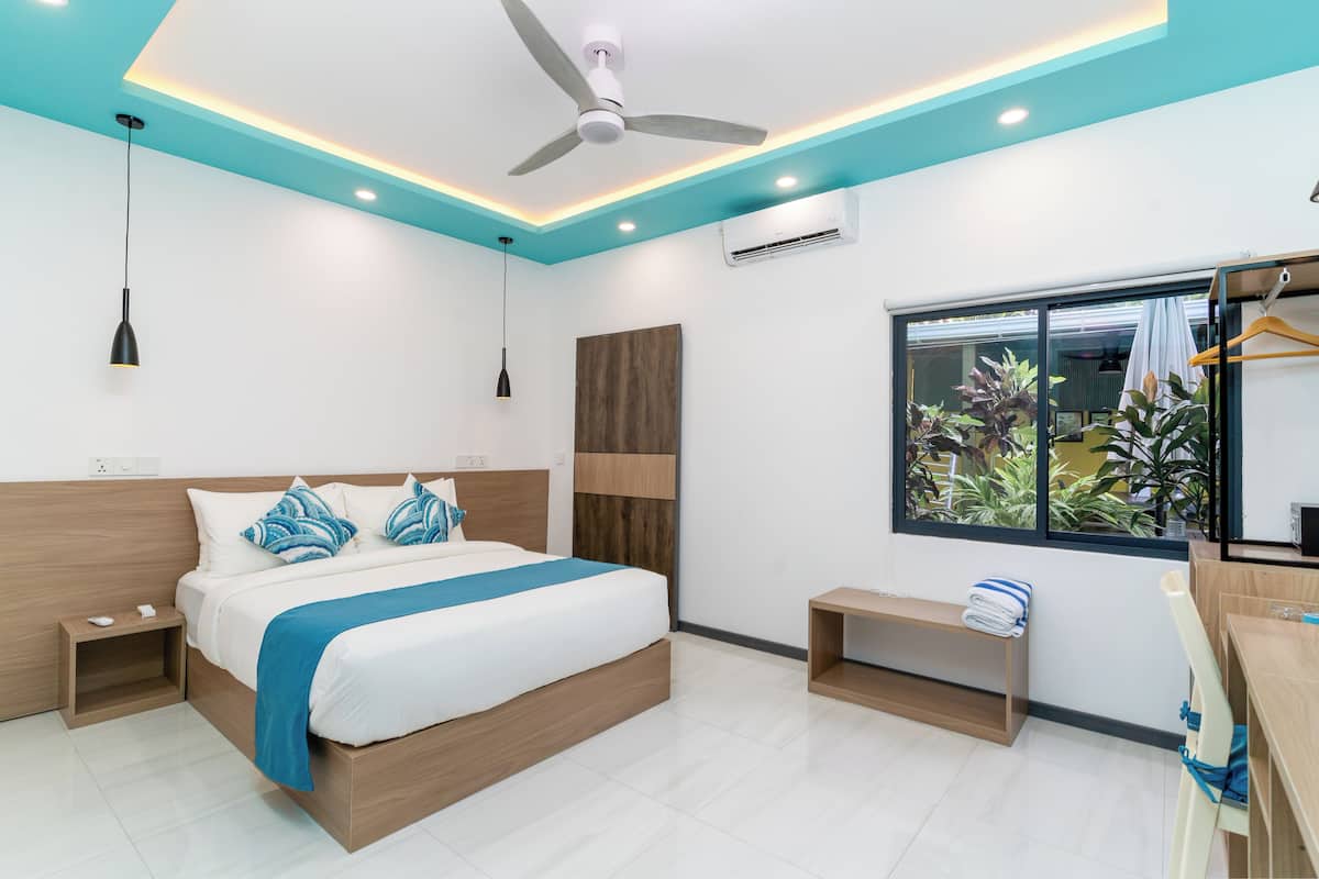 Un dormitorio moderno con cama, mesitas de noche, ventilador de techo, unidad de aire acondicionado, ventana con vistas y un banco.